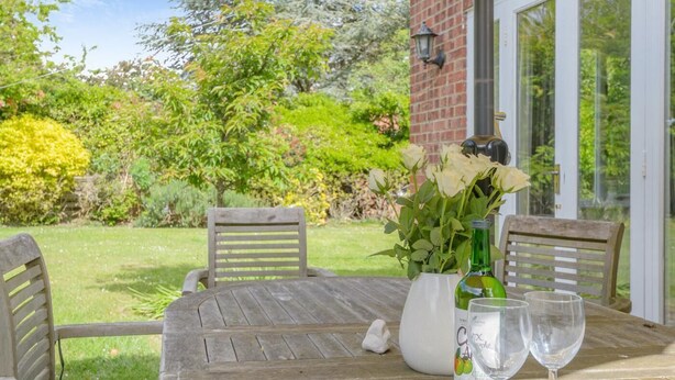 An outdoor wooden table with chairs, a vase with flowers, and two glasses. - 4 Bed in Old Hunstanton (oc-kt169) (Hunstanton)