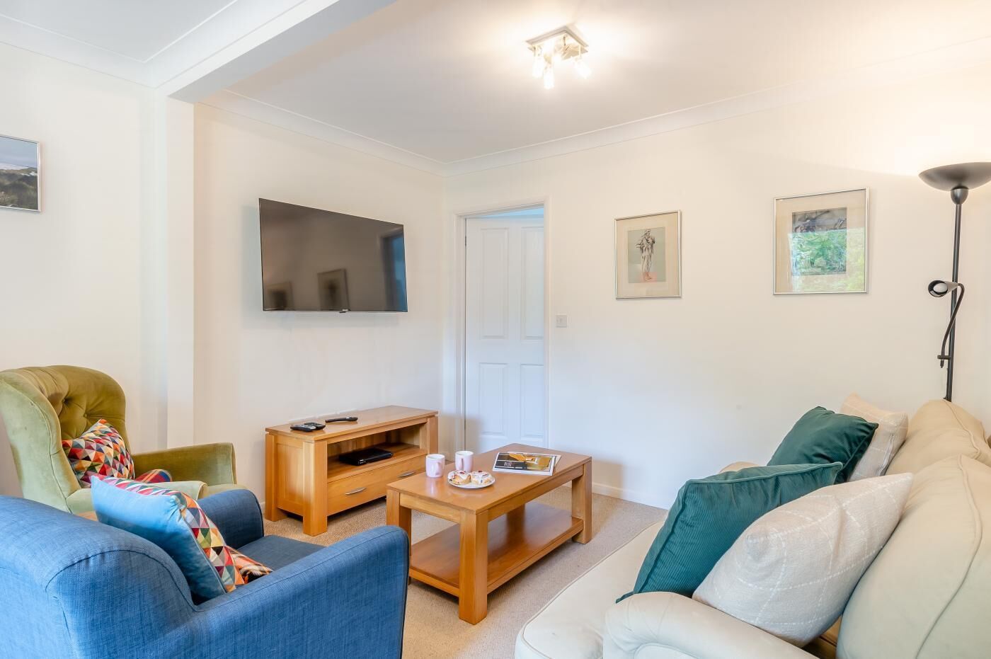 A living room with a sofa, armchair, coffee table, TV, and artwork on the walls.