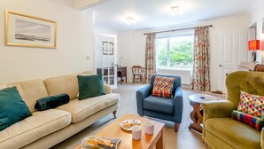 A living room with a sofa, armchair, coffee table, and a view of the outdoors through a window. - 4 Bed in Old Hunstanton (oc-kt169) (Hunstanton)