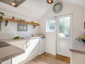 A kitchen with white cabinets, a wooden countertop, a dishwasher, a window with frosted glass, and a clock on the wall. - 1 Bed in Delabole (oc-65682) (Trewalder)