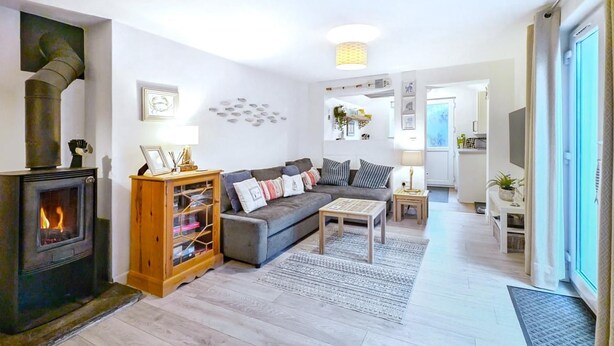 Ein modernes Wohnzimmer mit Kaminofen, grauem Sofa, Holzschrank und kleinem Tisch.