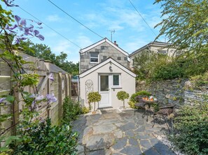 A small stone house with a white door, a small garden with a table and chairs, and a stone wall. - 1 Bed in Delabole (oc-65682) (Trewalder)