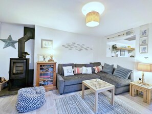 A cozy living room with a sofa, a small table, a bean bag, a bookshelf, and a fireplace. - 1 Bed in Delabole (oc-65682) (Trewalder)
