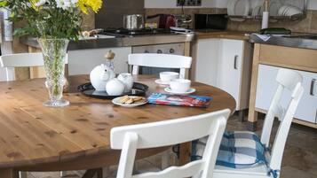 A dining area with a wooden table, white chairs, a vase of flowers, teapots, cups, and a magazine.