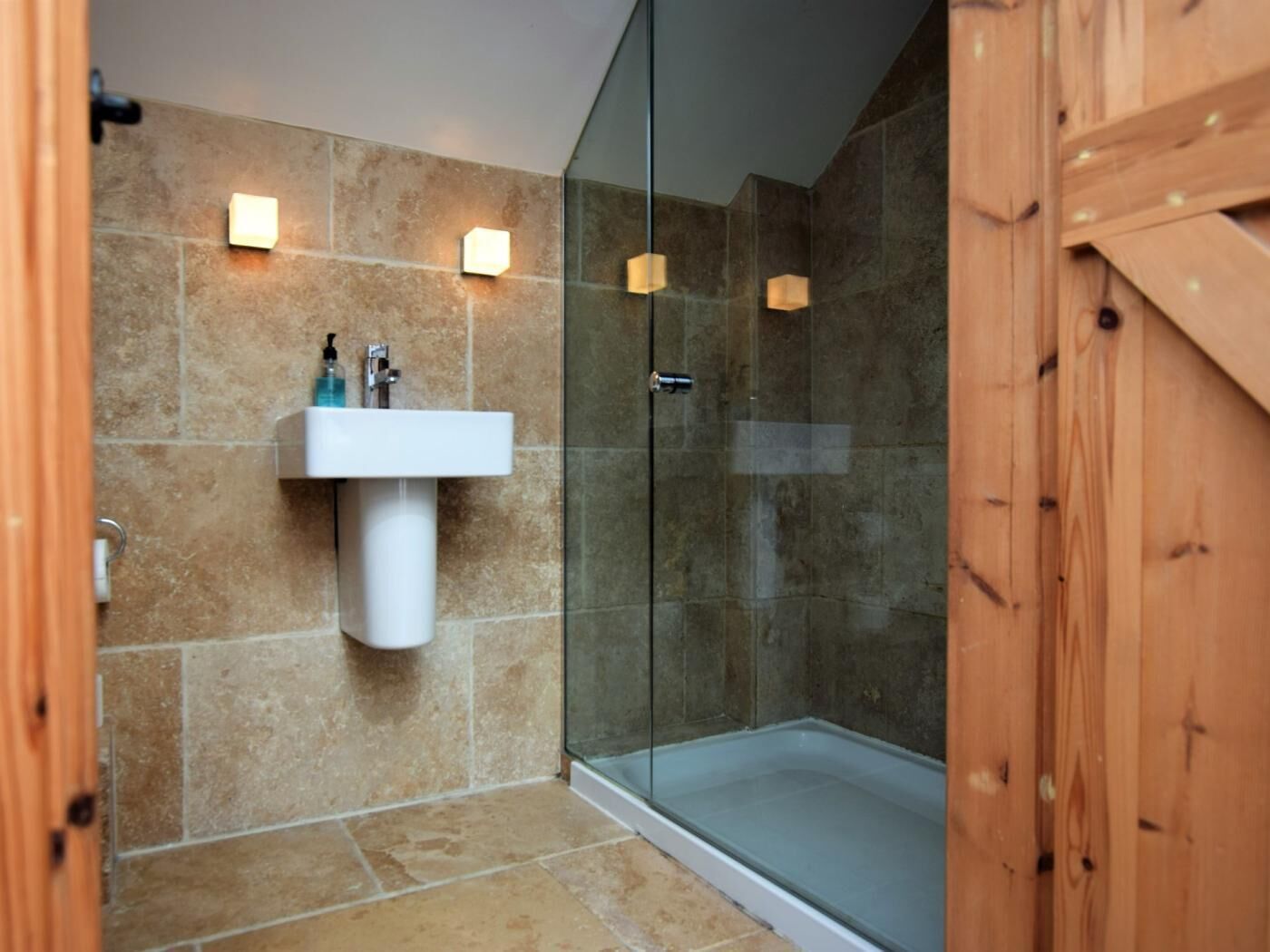 A bathroom with a glass shower enclosure, a white sink, and a wooden door.