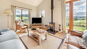 Ein Wohnzimmer mit Kamin, Sofa, Fernseher und Blick auf die Landschaft.