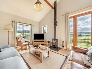 Uma sala de estar com lareira, sofá, TV e vista para o campo.