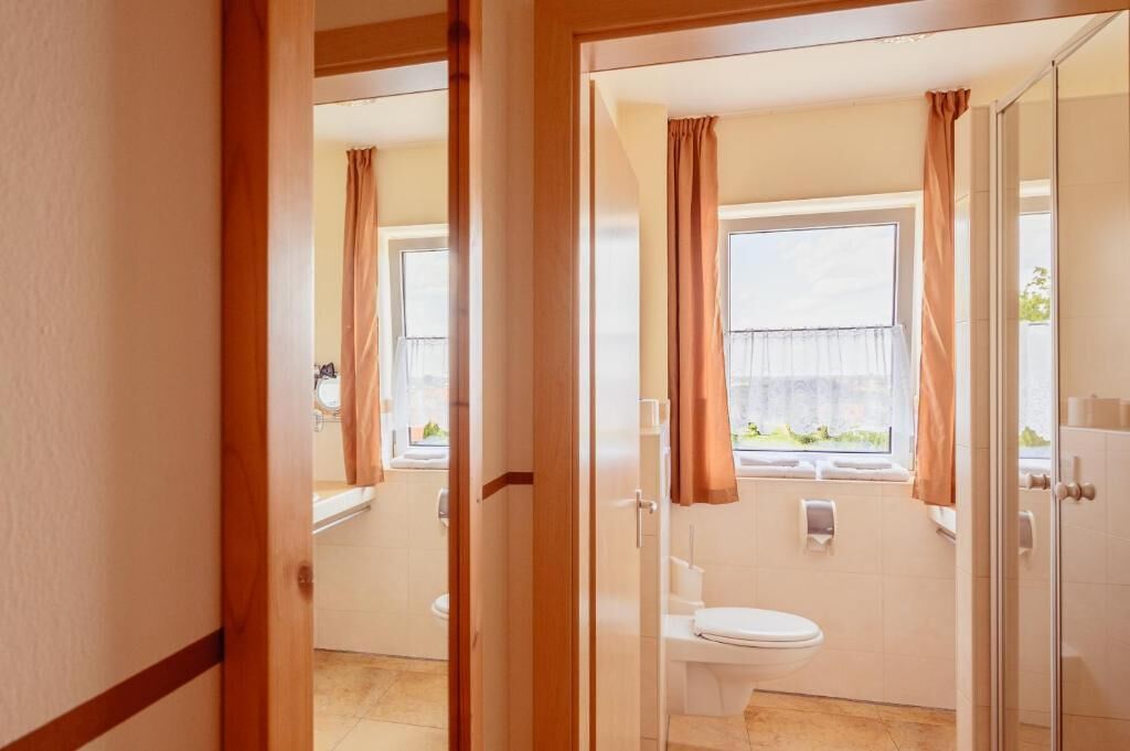 Ein Badezimmer mit Toilette, Dusche und einem Fenster mit Vorhängen.