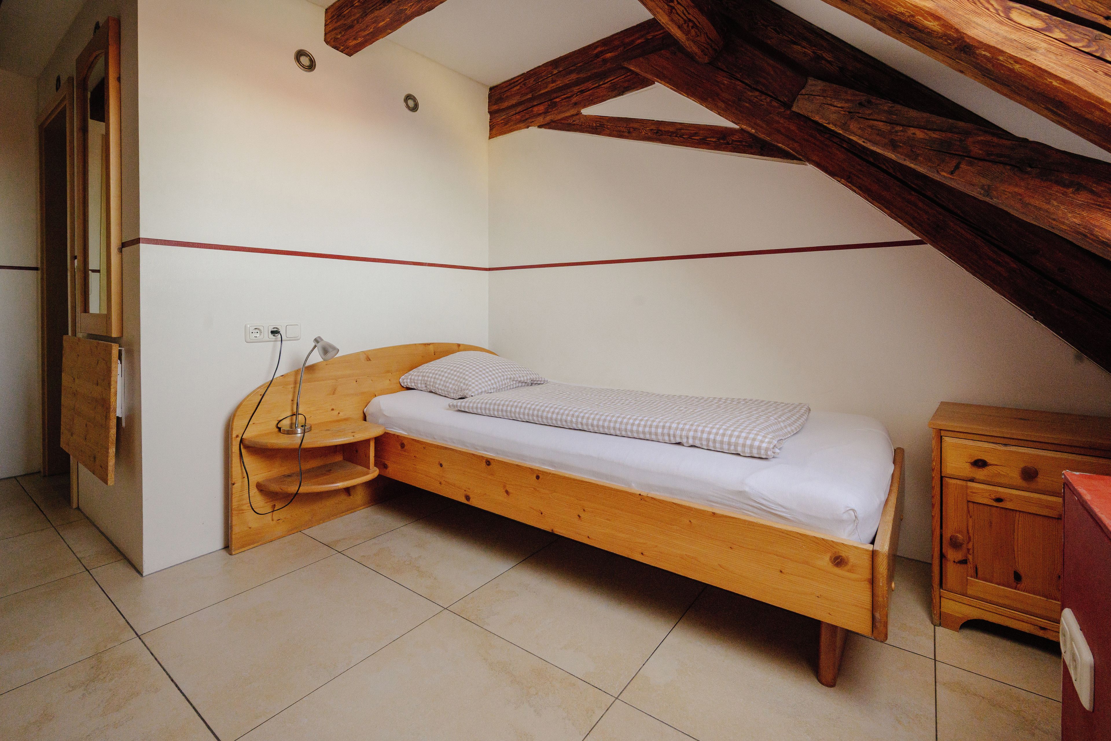 A small, single-bed room with a wooden bed, a nightstand, a mirror, and a wooden cabinet.