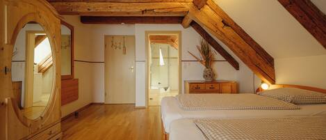 A bedroom with a sloped ceiling, wooden beams, a large mirror, a bed with checkered bedding, and a nightstand with a lamp.