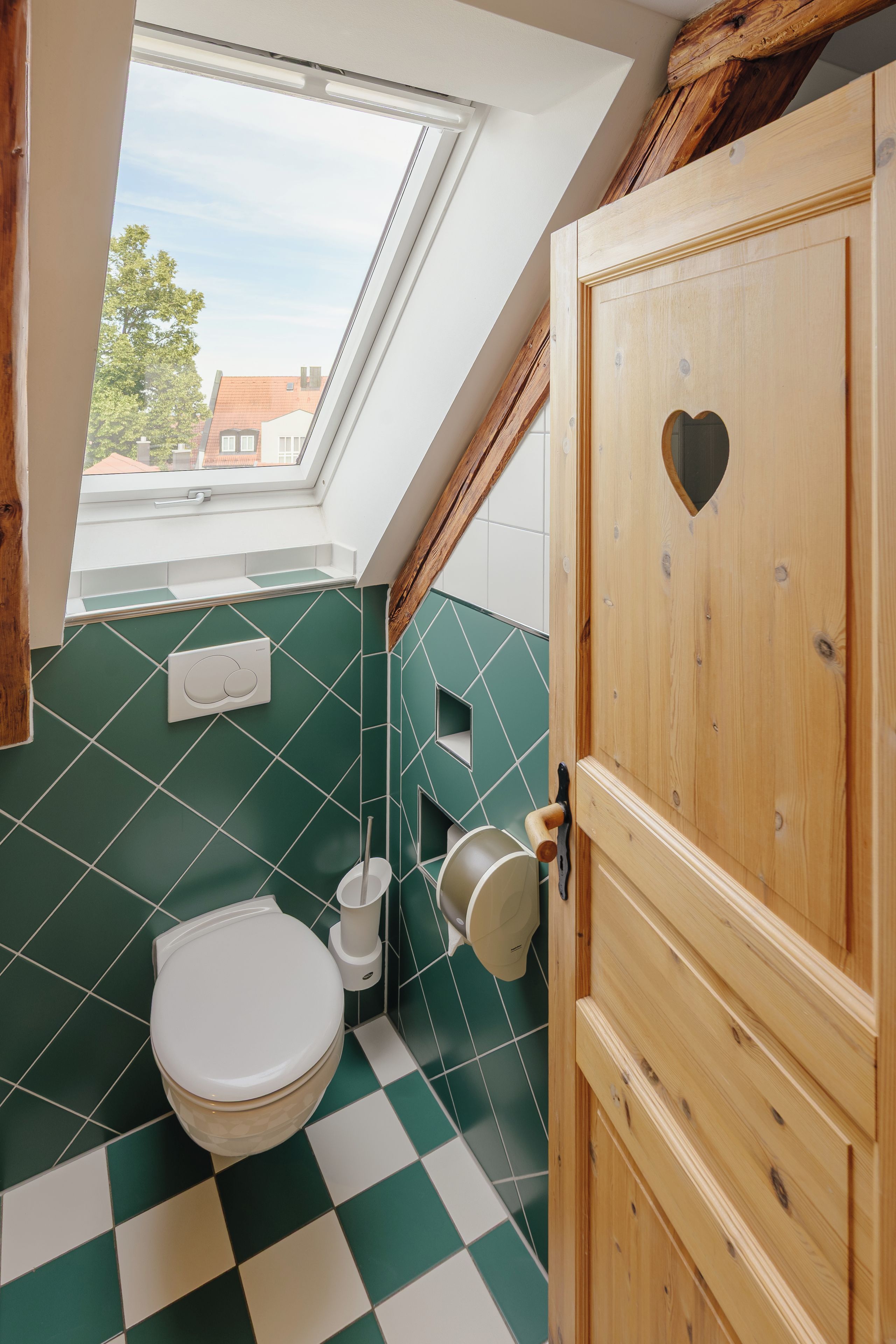 A small bathroom with a skylight, a toilet, and a wooden door with a heart-shaped cutout.