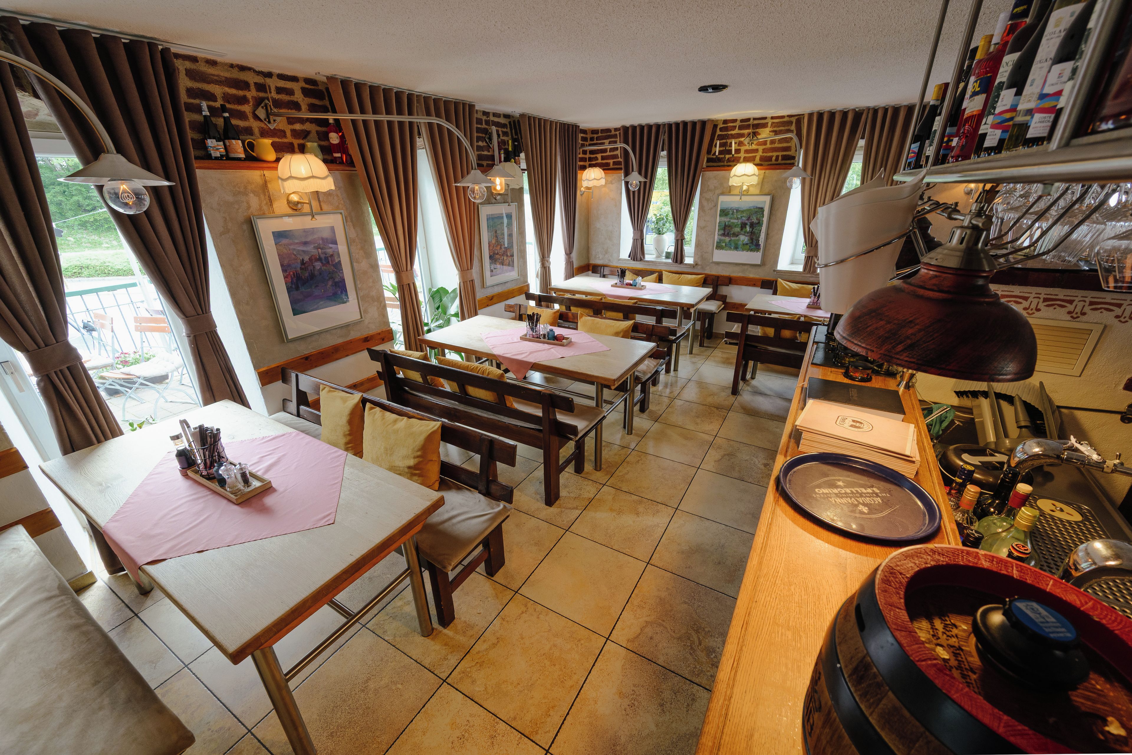 A restaurant with multiple tables and benches, a bar area with bottles, and artwork on the walls.