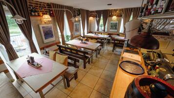 A restaurant with multiple tables and benches, a bar area with bottles, and artwork on the walls.