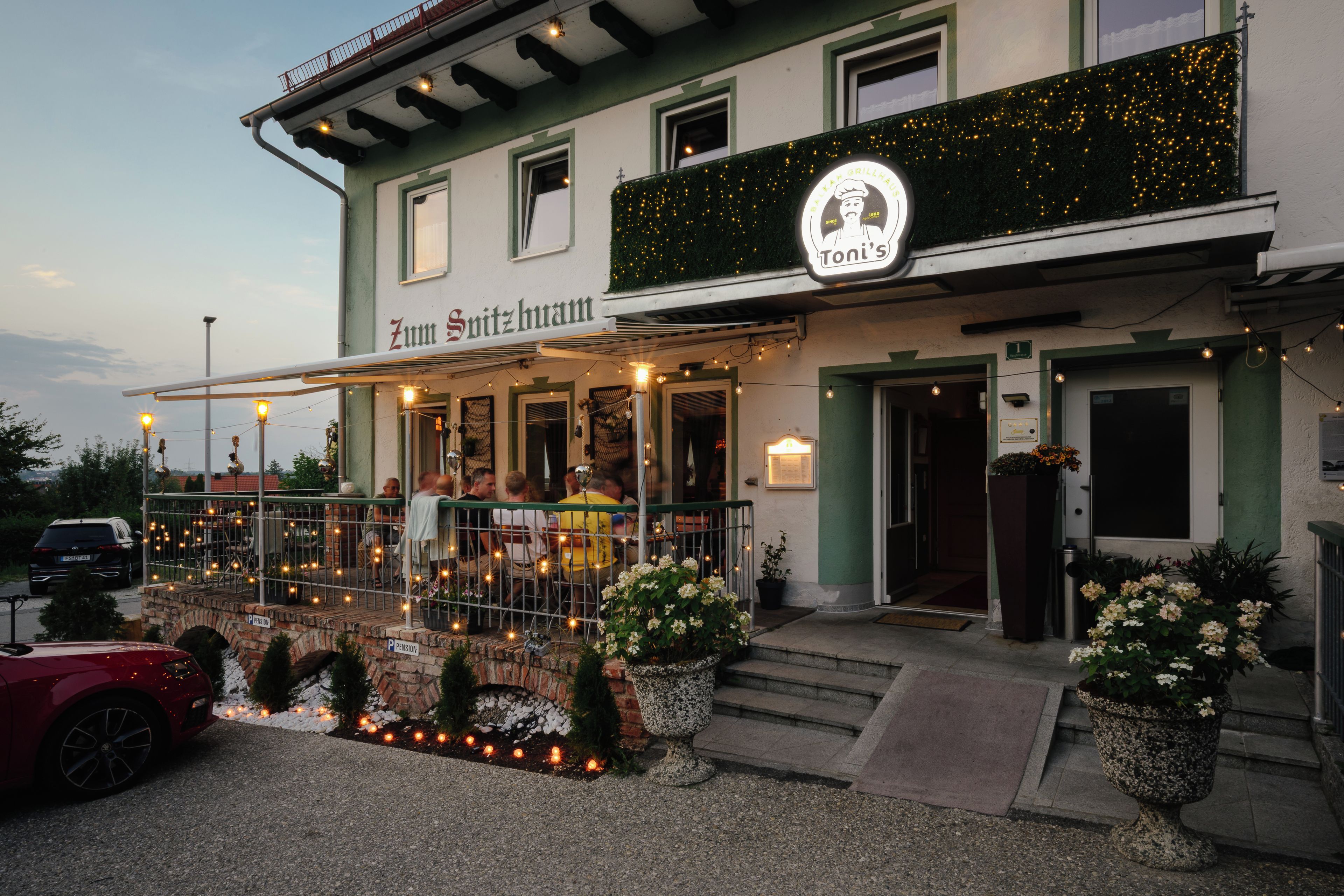 Ein Restaurant mit Außenbereich, einem Schild mit der Aufschrift 'Zum Spitzhaus' und dem Schriftzug 'Toni's' über dem Eingang.