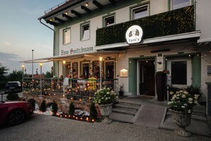 Restaurante com mesas ao ar livre, uma placa com a inscrição 'Zum Spitzhaus' e o logotipo 'Toni's' acima da entrada.