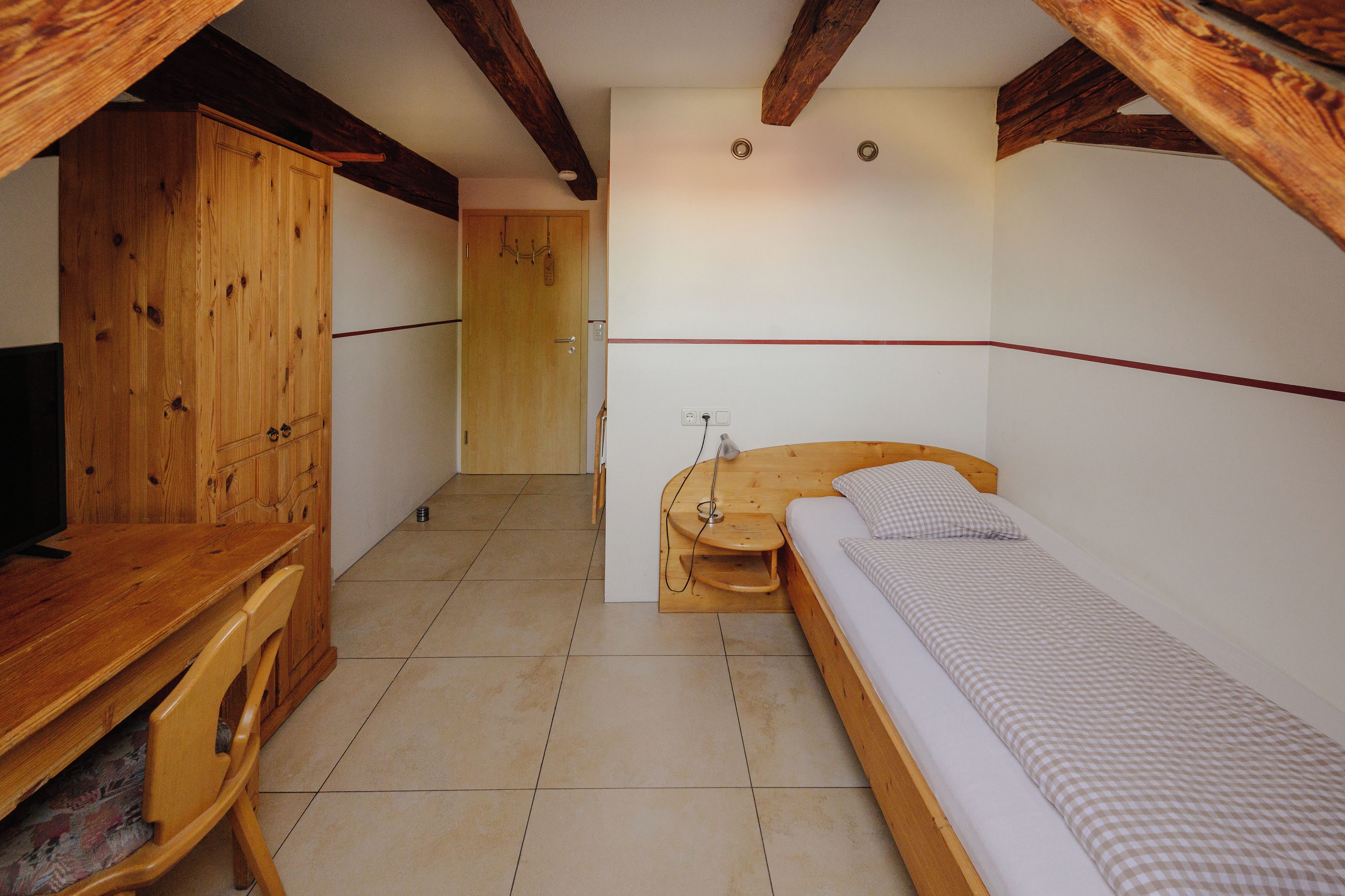 Een kleine, compacte kamer met een houten bed, een bureau van hout en een kledingkast.