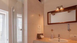 A bathroom with a glass shower, a sink with a mirror above, and a window with curtains.
