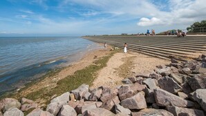 En strand med en stenig förgrund, en sandstrand och en klar himmel.