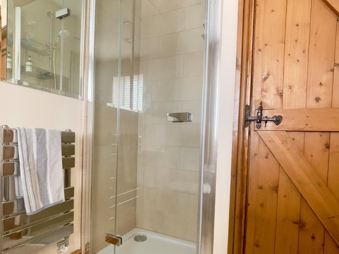 Une salle de bain avec une douche à parois de verre, une porte en bois et un porte-serviettes avec des serviettes.