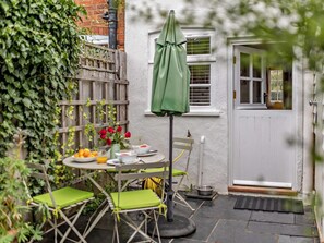 A patio with a table, chairs, a green umbrella, and a white door. - 1 Bed in Tenterden (oc-66342) (Tenterden)