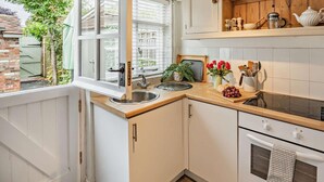 A kitchen with a window, a sink, a stove, and a countertop with a plant and a vase of flowers. - 1 Bed in Tenterden (oc-66342) (Tenterden)