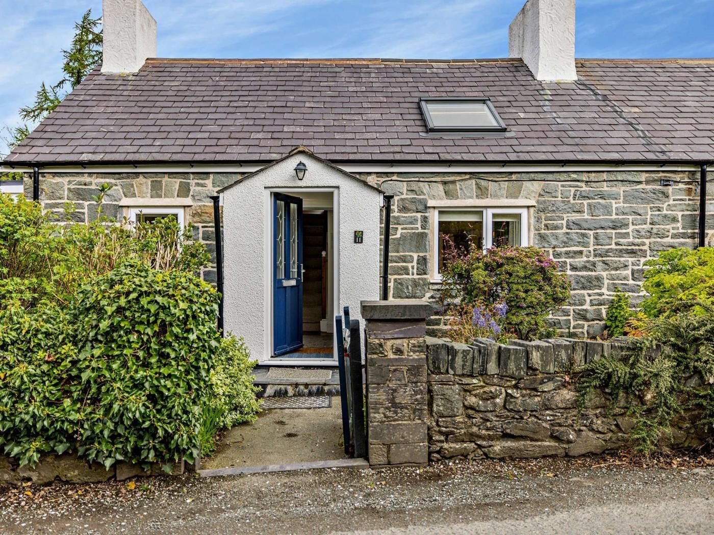 Une petite maison en pierre avec un toit recouvert de tuiles sombres, une porte bleue et une petite fenêtre.