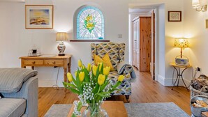 A cozy living room with a patterned armchair, a wooden side table, a vase of flowers, and a stained glass window. - 2 Bed in Bangor (oc-66276) (Llanddeiniolen)