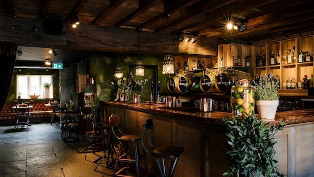 A rustic bar area with wooden beams, a bar counter, stools, and a variety of bottles and jars. - 2 Bed in Newcastle Upon Tyne (oc-66305) (Otterburn)