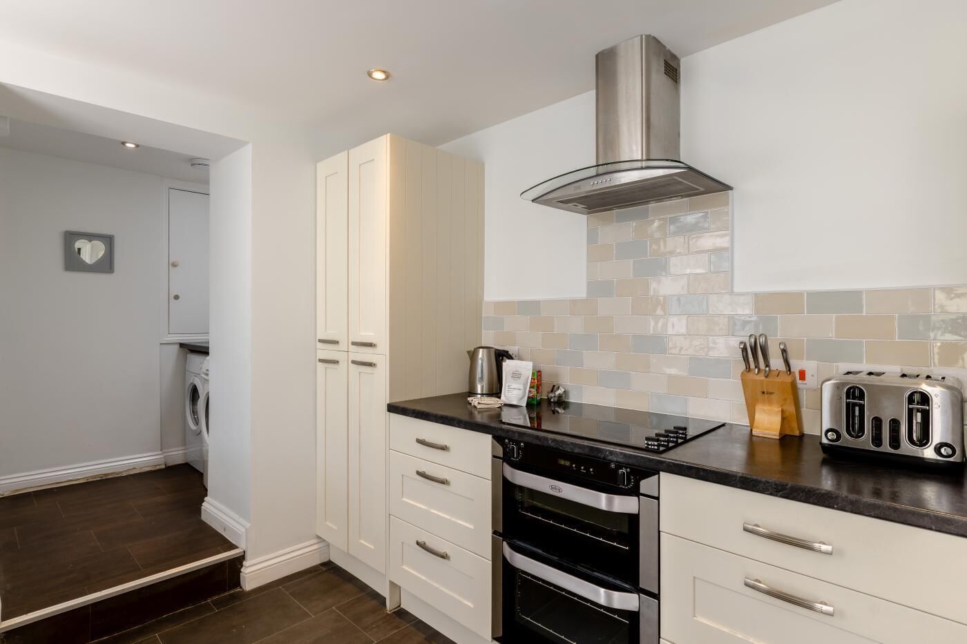 A modern kitchen with white cabinetry, a stainless steel range hood, a dishwasher, an oven, and a toaster.