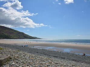 Ein Strand mit Kieselsteinen, einem Sandufer und hügeliger Landschaft im Hintergrund.