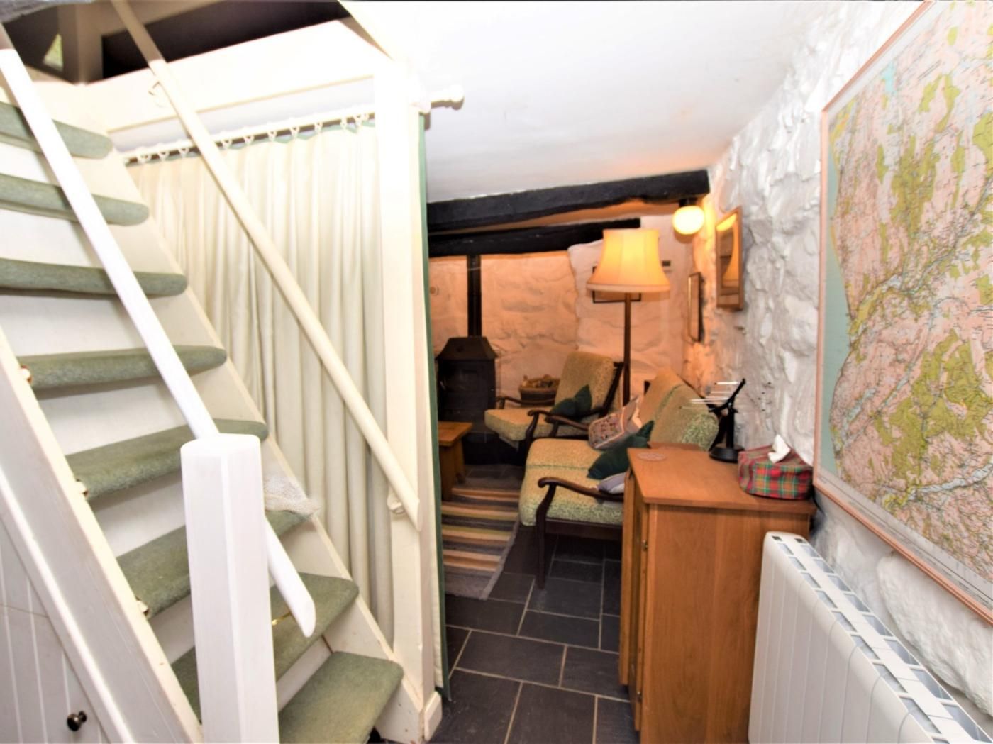 A staircase leading to a cozy room with a stone wall, a map, and a table with a lamp.