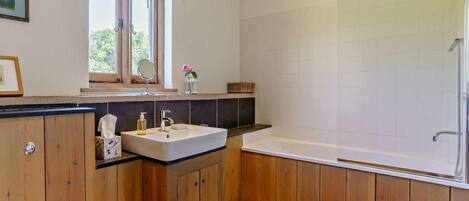 Un baño con armarios de madera, un lavamanos blanco, un espejo, un ventanal y una zona de ducha.