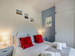 A hotel room with a bed, two red pillows, a nightstand with a lamp, a bedside table, and a wall with three framed pictures. - 3 Bed in Norwich (oc-66597) (Trimingham)