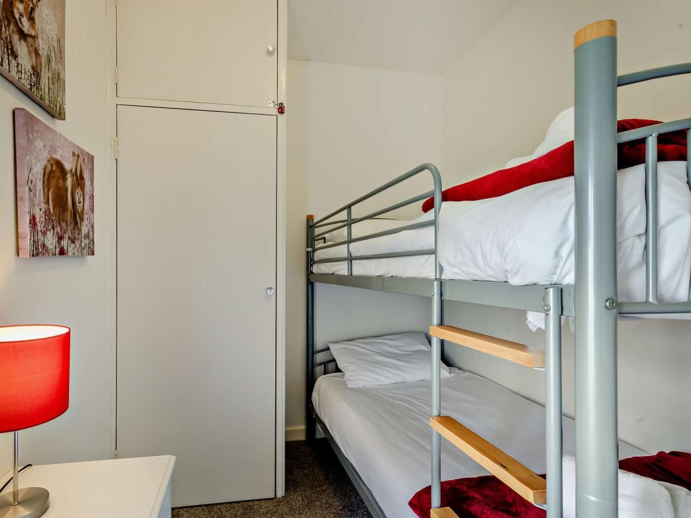 A bunk bed room with a door, a desk with a lamp, and two paintings on the wall.