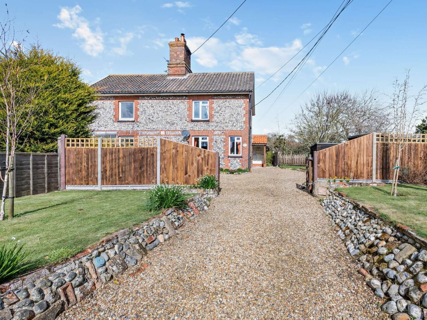 A two-story stone house with a gravel driveway leading to a wooden gate.