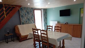 Un coin repas avec une table et des chaises, un canapé, un escalier, un radiateur et un téléviseur fixé au mur.