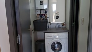 Une petite buanderie équipée d’un lave-linge, d’un sèche-linge et d’un chauffe-eau.