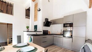 Moderni keittiö, jossa on sisäänrakennettu uuni, pesuallas ja ruokailutila, jossa on pöytä kahdelle.