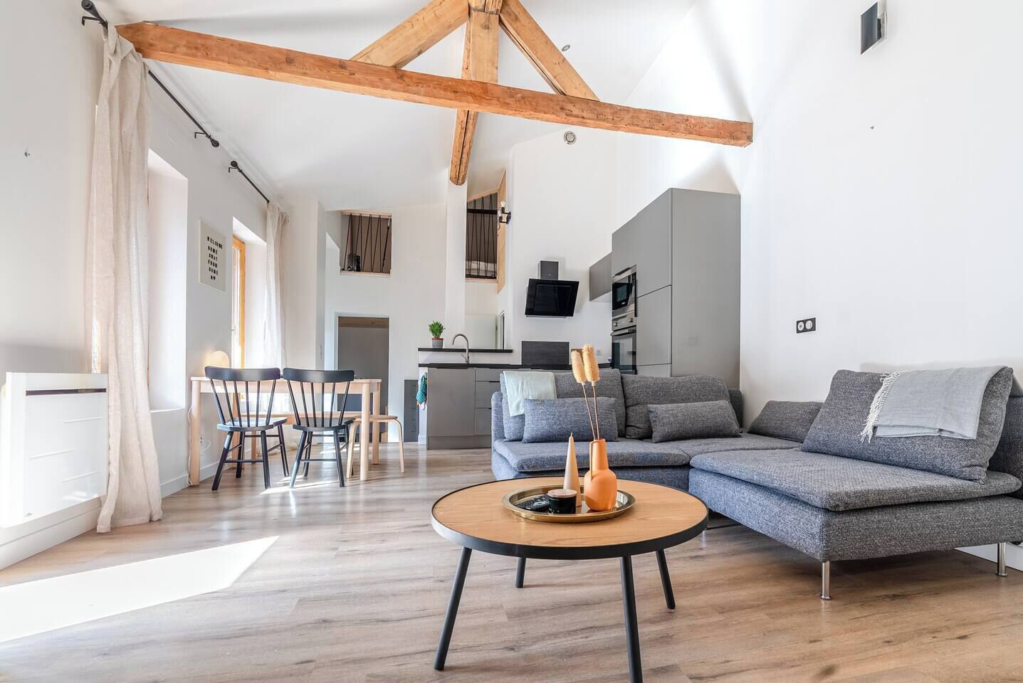 A modern living room with a wooden ceiling, a grey sectional sofa, a round coffee table, and a dining area with a table and chairs.