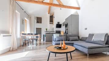 A modern living room with a wooden ceiling, a grey sectional sofa, a round coffee table, and a dining area with a table and chairs.