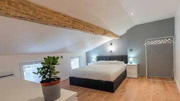 A bedroom with a sloped ceiling, a bed, bedside tables, a plant, and a hanging laundry rack.