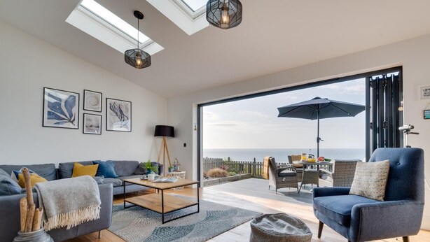 Een moderne woonkamer met een bank, salontafel en stoelen, een balkon met uitzicht en een groot raam.