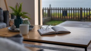 Een houten tafel met een boek, brillen, een witte mok en een groene plant.