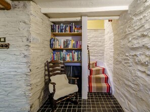 A narrow hallway with a wooden chair, a bookshelf filled with books, and a striped carpeted staircase. - 2 Bed in Ambleside (oc-72378) (Hawkshead)