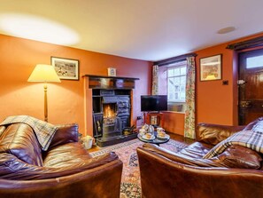 A cozy living room with a fireplace, leather sofas, a television, and a window with curtains. - 2 Bed in Ambleside (oc-72378) (Hawkshead)