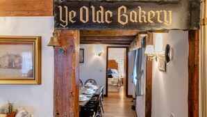 Ein Flur mit einem rustikalen Holzschild, auf dem 'Ye Olde Bakery' steht, und ein Essbereich mit einem langen Tisch, der für eine Mahlzeit gedeckt ist.