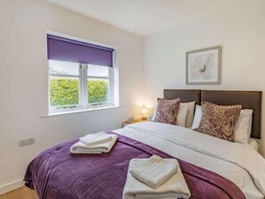 A bedroom with a bed, pillows, a window with a view, a bedside table with a lamp, and a framed picture on the wall. - 2 Bed in Louth (oc-72401) (Fotherby)