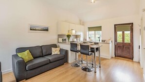 Eine moderne Küche mit Essbereich, ein graues Sofa mit grünem Kissen und ein Holzboden.