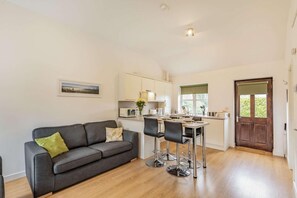 A modern kitchen with a dining area, a grey sofa with a green pillow, and a wooden floor. - 2 Bed in Louth (oc-72401) (Fotherby)