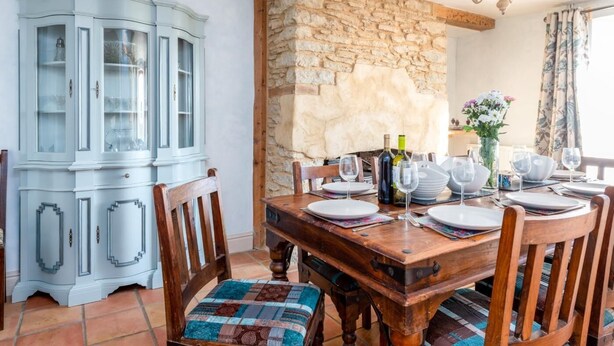 A dining area with a stone wall, a wooden table set for four, and a light blue cabinet with glass doors. - 4 Bed in Gillingham (oc-80670) (West Stour)